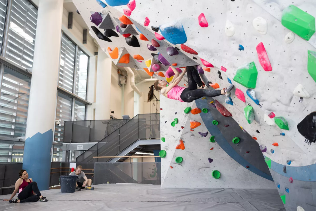 Nainen kiipeilee jyrkällä boulderseinällä, jossa on paljon värikkäitä otteita.